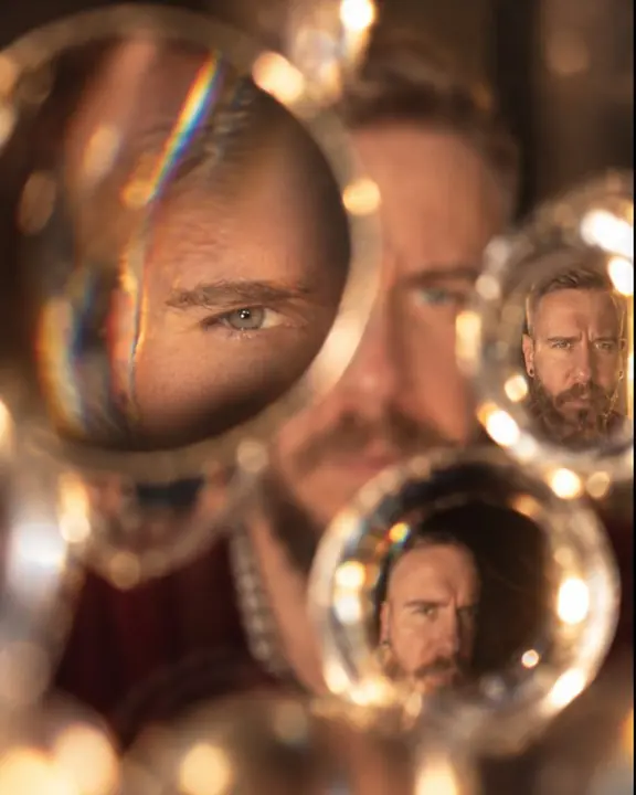 Loose lenses at different distances magnify parts of a bearded man's face and shrink others in warm light