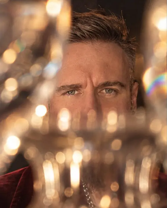 A bearded man's eyes seen directly between blurred, glowing glass rims in warm amber light
