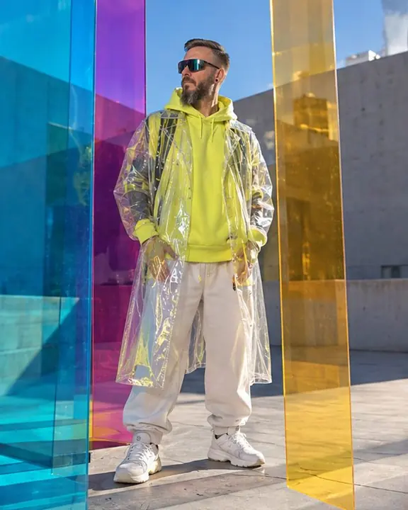 Full-length man in a clear PVC trench and acid-yellow hoodie behind three panels, each a different color