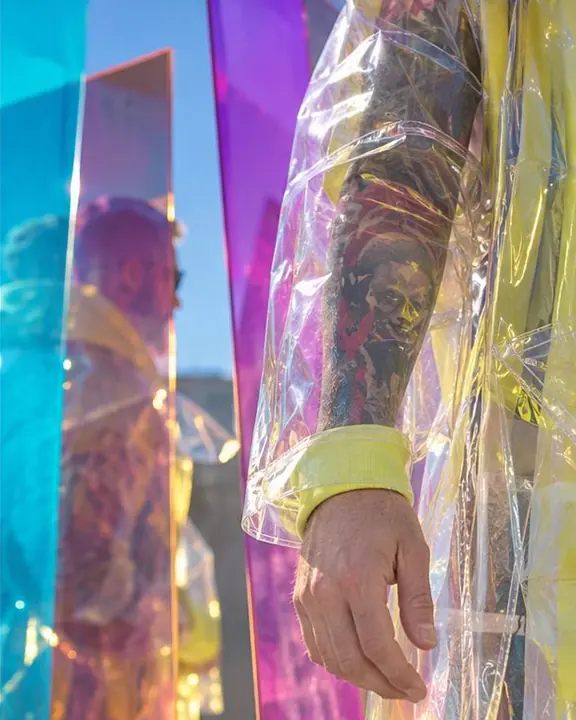 Detail of a clear PVC sleeve over an acid-yellow hoodie, seen through overlapping cyan and gold layers