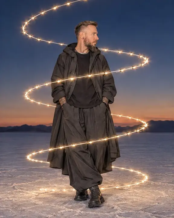 A helix of warm light spirals up around a bearded man on a salt flat, his face frozen sharp by flash