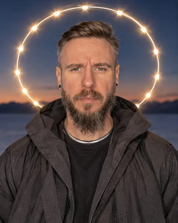 Waist-up shot of a bearded man looking into the lens, a halo ring of light behind his head on a blue sky