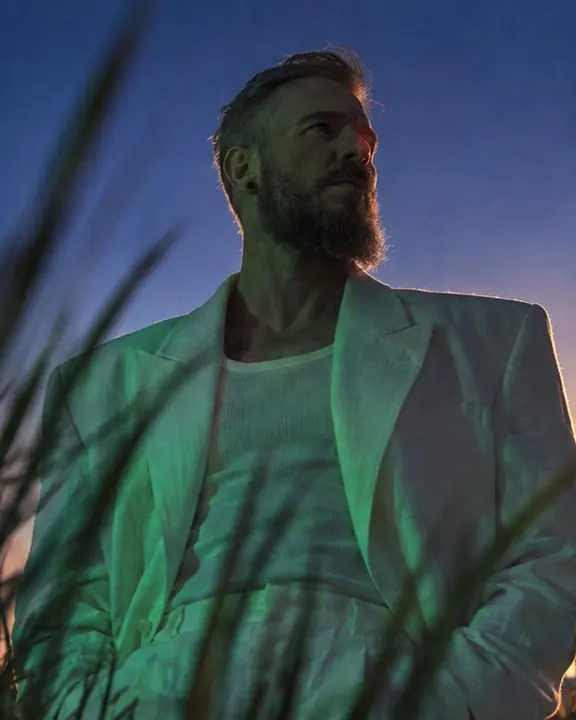 Waist-up man in white linen, emerald green light on the lapels, his face mostly in shadow at blue hour