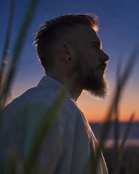 Profile of a bearded man rimmed by the last sunset light, blurred dune grass in the foreground