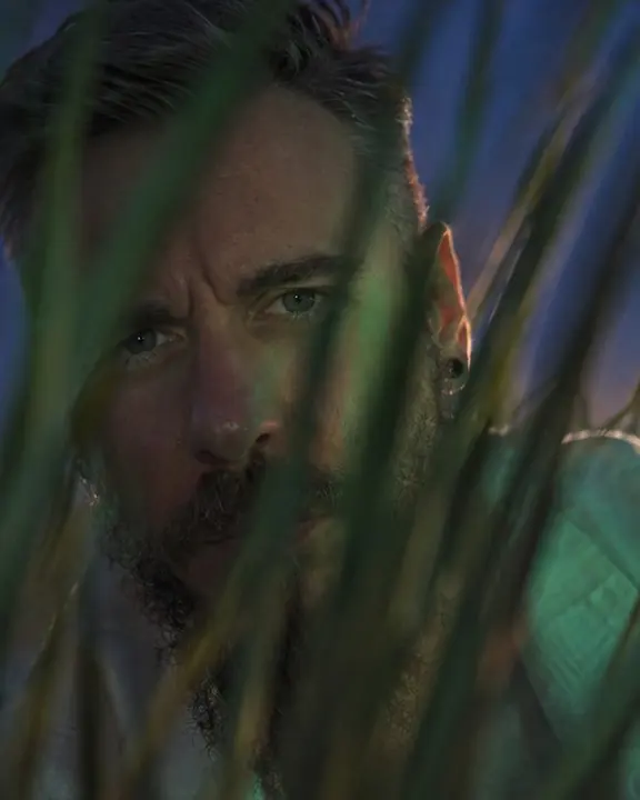 Close-up of a bearded man's eyes catching a little green light between soft blades of grass