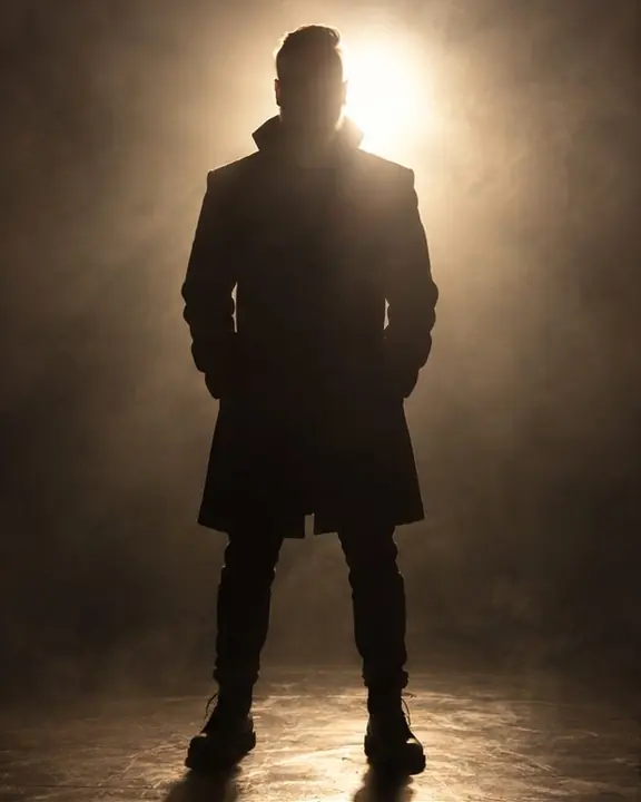 A man's black silhouette in a halo of haze, a bright backlight flaring just above his shoulder