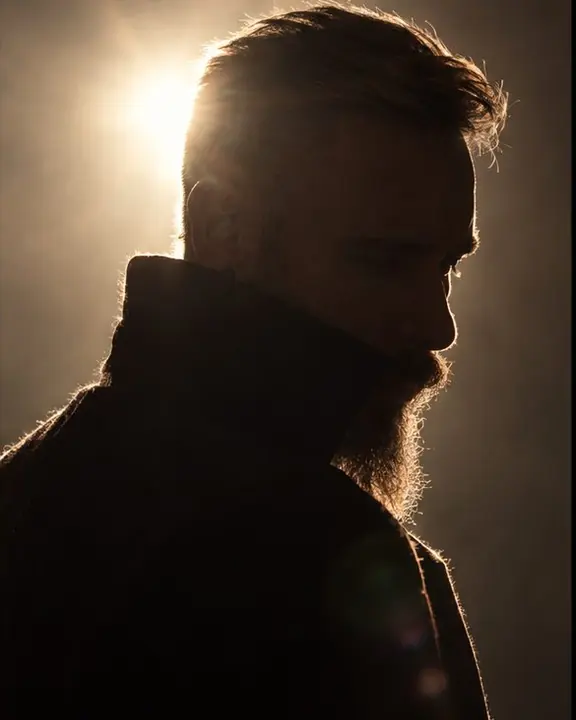 The high collar of a sculptural black coat glowing with a thin line of rim light against pure black