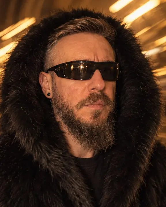 Close-up of a fur hood framing a bearded man's face, amber escalator lamps streaking behind him