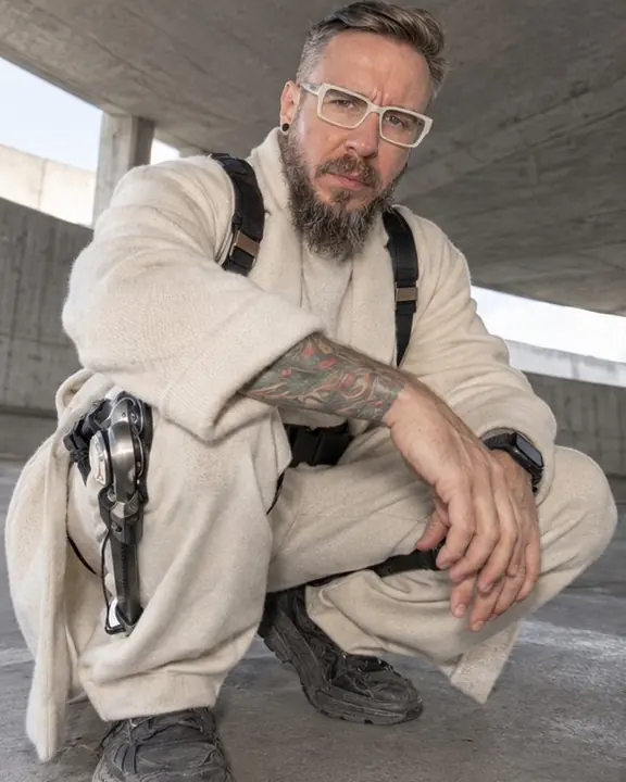 A bearded man crouches close to an ultra-wide lens, titanium knee hinges folding over wide cream trousers