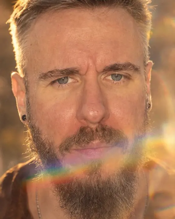 Close-up of a bearded man looking into the lens, a band of rainbow light leak crossing his lower face