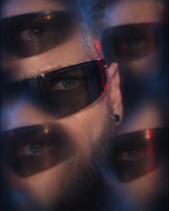 Close-up of a man's eye behind black visor glasses, the same eye repeated four times around it in blue light