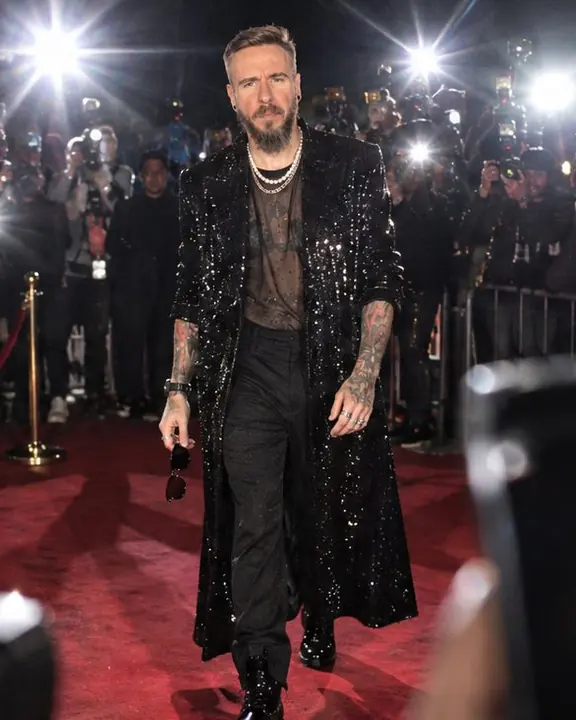 Full-length of a man on a red carpet, several hard shadows fanning on the wall behind, flare stars around him