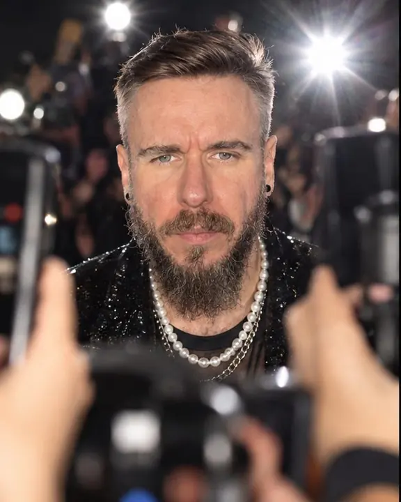 A bearded man stops and looks straight into one lens through a forest of raised hands and phones
