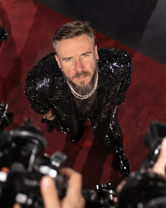 High-angle view from a press platform of a man in a sequin coat looking up into dozens of flashes