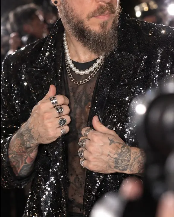 Hands with silver rings hold a black sequin coat closed, sparkling under a dozen camera flashes