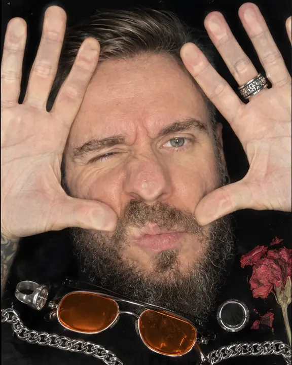 Both palms flat on scanner glass framing a bearded face, sunglasses with neon-orange lenses lying across