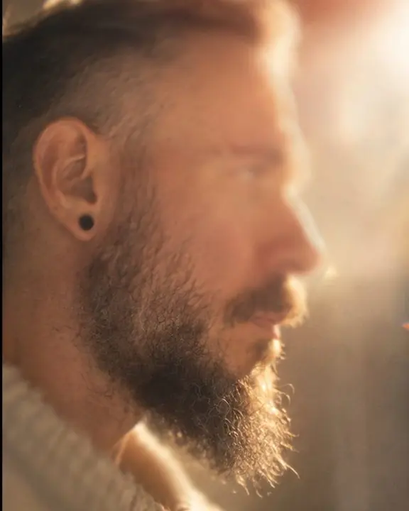 Profile of a bearded man with the beard edge sharp and the eye soft, a milky light leak washing half the frame