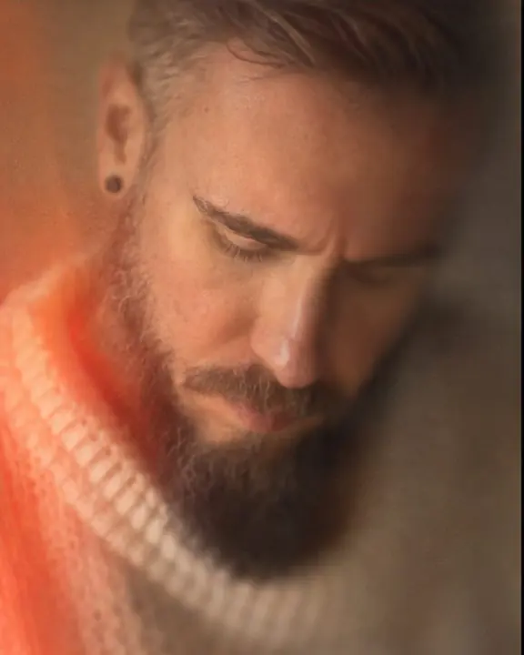 A bearded man looks down, a thin sliver of sharp focus on the bridge of his nose and the rest in warm blur