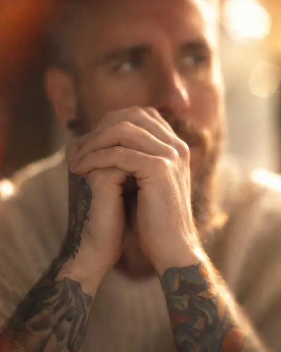 A man's fingers sharp near his face while the face behind melts into soft, warm amber blur