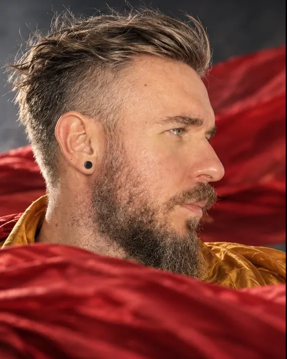 Close-up of a bearded man turning against the wind, hair pushed back, crimson silk flying past in front