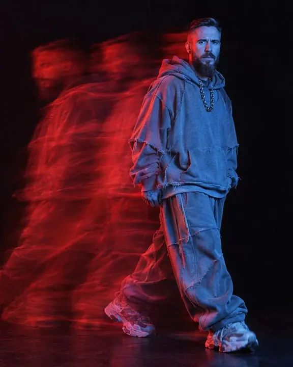 Full-length bearded man frozen sharp in blue light on the right, a smeared red ghost of his step streaming left