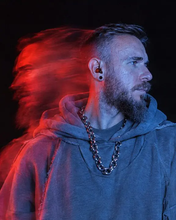 A bearded man in a gray double hoodie, head turned, his face sharp in blue with a red ghost of the turn behind