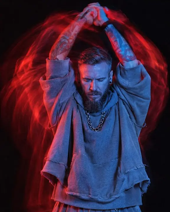 A man with arms swung overhead, sharp in blue, red arcs tracing the path of his arms against a black background