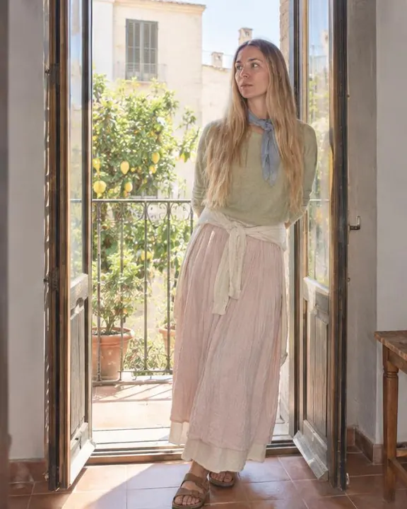 A woman with long blond hair leans in an open balcony doorway, backlight rimming her pistachio knit, face soft in fill flash