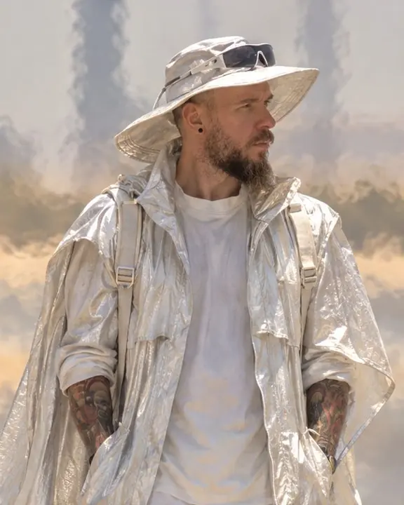 Waist-up telephoto of a bearded man under a wide-brimmed sun hat, his outline shimmering in the heat