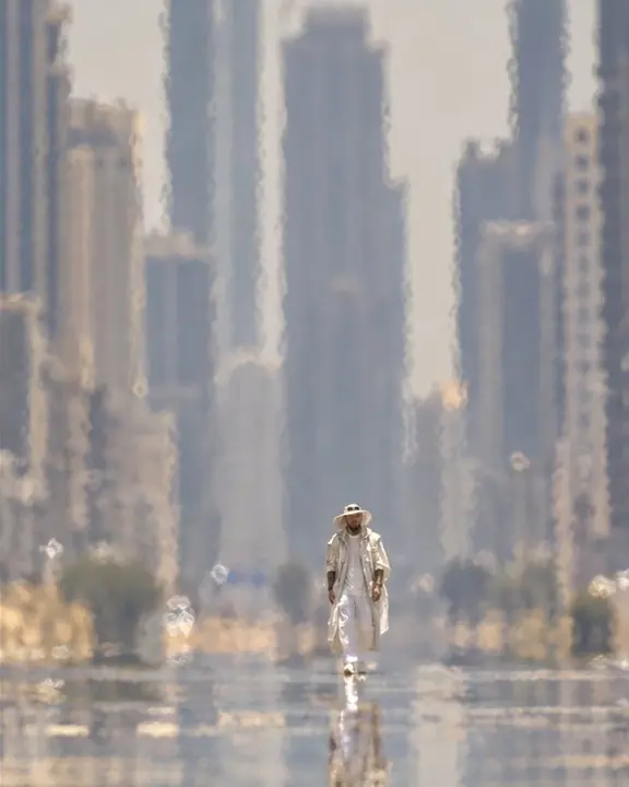A man in white stands tiny between compressed high-rise facades, heat waves visible in the air