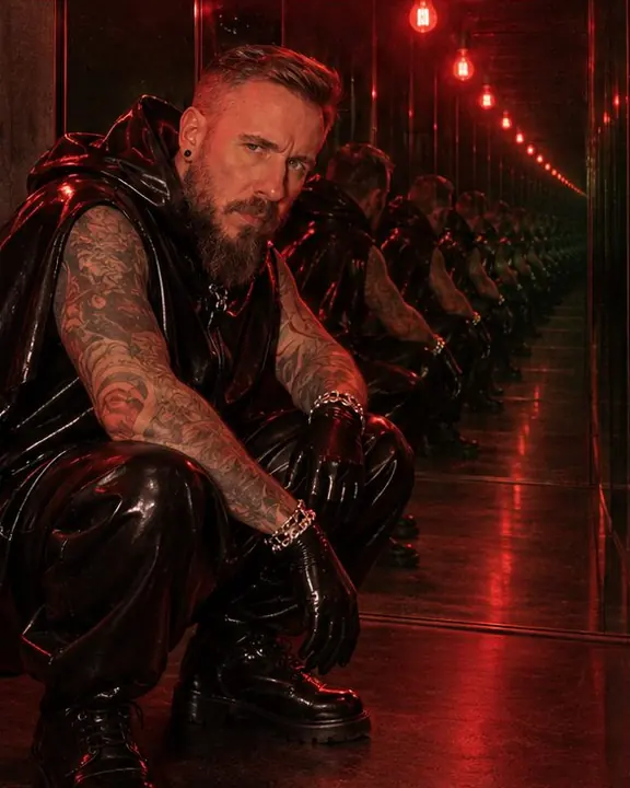A bearded man crouching between two mirrors, his infinite copies curving slightly into the distance