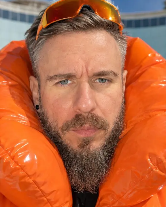Close portrait of a bearded man nested in a puffed orange pillow collar, looking into the lens
