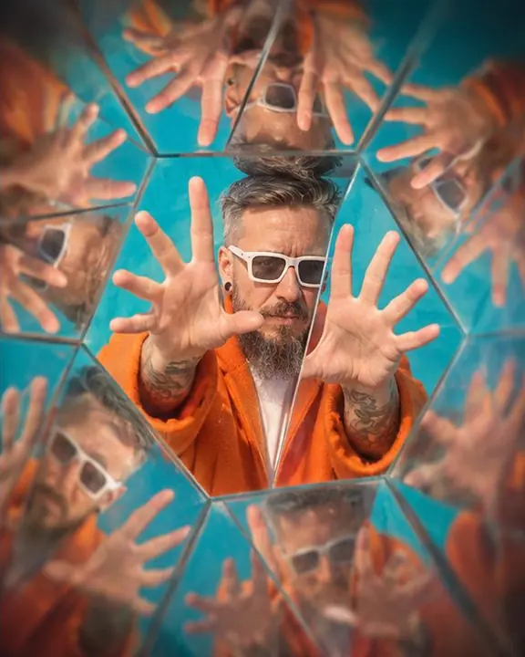 Raised hands repeated into a star shape around a bearded man's face against a bright turquoise wall