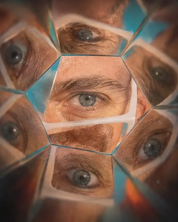 A man's eye at the center of the frame, mirrored outward into a flower of eyes with orange accents
