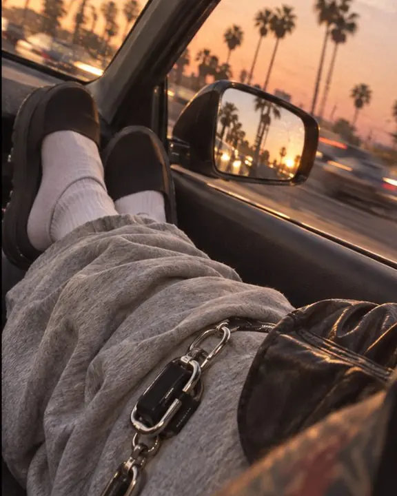Black leather jacket sleeve on a sun-warmed car door, blurred palm trees streaking in the side mirror