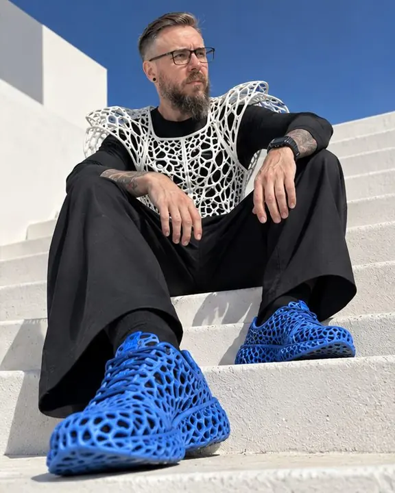 Low angle on white steps, electric blue 3D-printed lattice sneakers large in the foreground, a man above