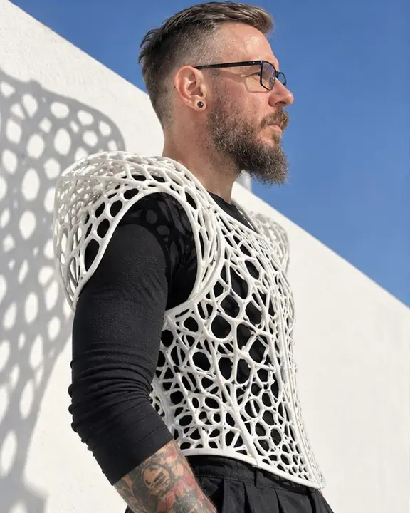 Waist-up profile of a man, sculptural lattice shoulder pieces silhouetted against a bright sky