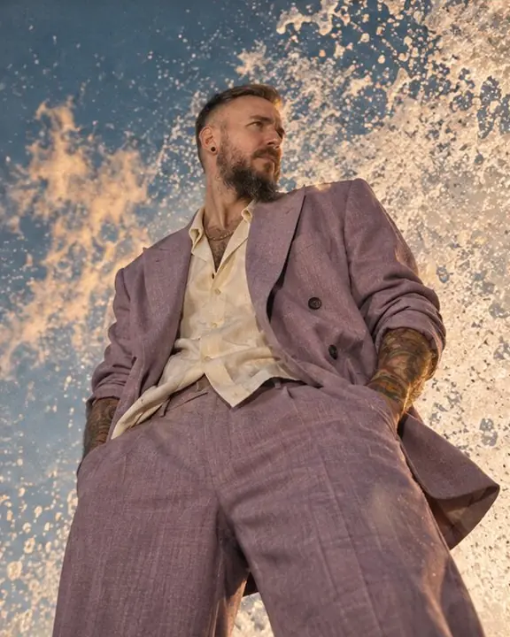 Low-angle shot of a man in lilac on the seawall with a breaking wave rising high above him