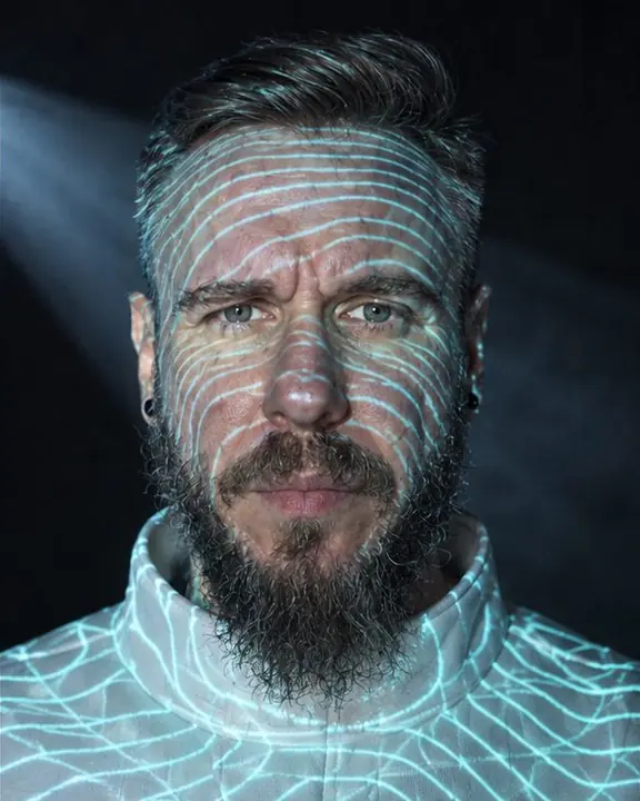 Head and shoulders of a bearded man with dense cyan contour lines projected across his face and white collar