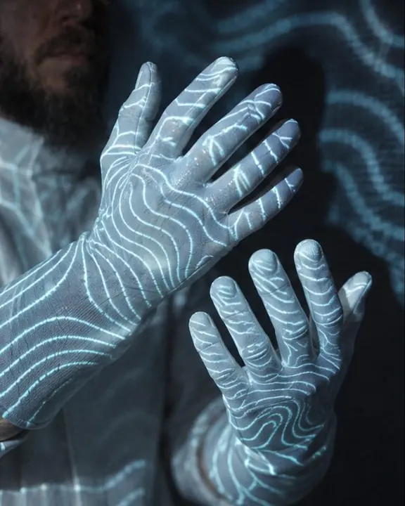 White-gloved hands with projected cyan contour lines flowing across the fingers in a dark room