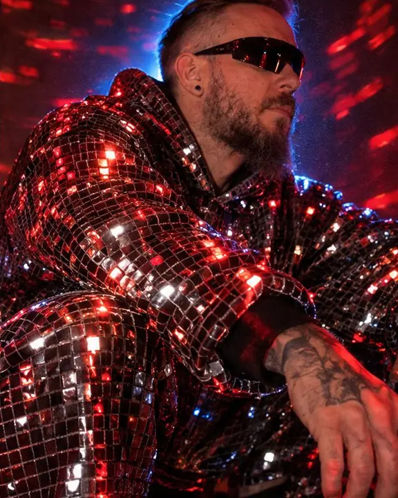 Detail of small mirror tiles on a hoodie sleeve reflecting long red arcs of light in the dark