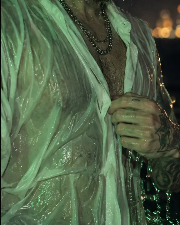 Detail of wet white shirt fabric and silver chains glinting in green ring flash light at night