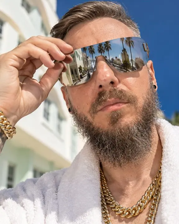 Close-up of a bearded man in mirrored shield sunglasses reflecting a sunny Miami Beach street