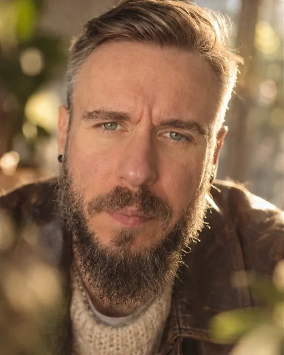 Close portrait of a bearded man looking into the lens, eyes sharp, the frame edges dissolving into soft swirl