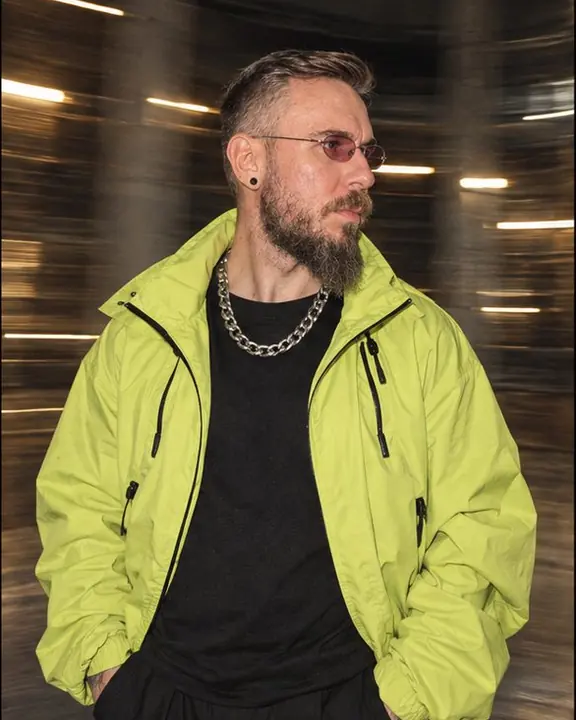 Waist-up shot of a bearded man, warehouse columns bent into curved streaks around his sharp figure