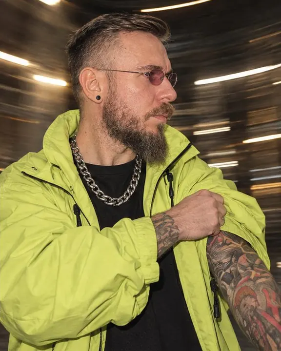 A heavy silver chain and acid-lime sleeve in sharp focus, circular streaks of warm light swirling behind