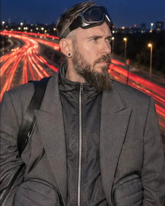 Waist-up bearded man with ski goggles pushed up on his forehead, a river of red traffic light behind his head