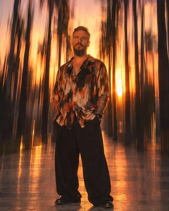 Full-length man as a vertical stroke against sunset sky streaks in pink and gold, palms blurred