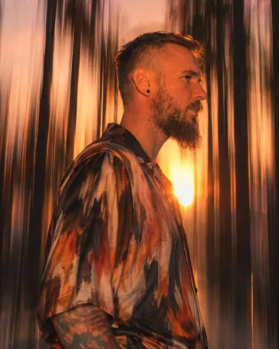Profile of a bearded man in a rust-and-ink printed silk shirt, the print stretched into vertical streaks