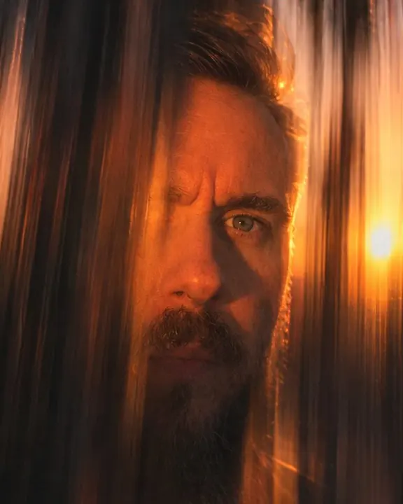 Close-up of a bearded man's eyes in orange light, everything around dragged into vertical strokes